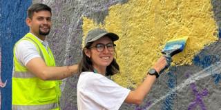 Foto de dos jóvenes realizando labores de voluntariado pintando una pared con rayones de aerosol.