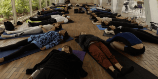 Imagen de varias personas acostadas ene l suelo tomando una clase de yoga
