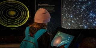 Imagen de niña de espaldas interactuando en pantalla en el Planetario