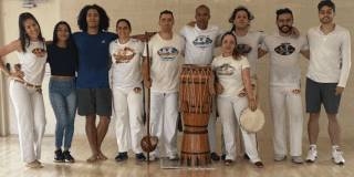 Imagen de varios participantes de una clase de capoeira de los cuales uno de ellos porta un tambor 