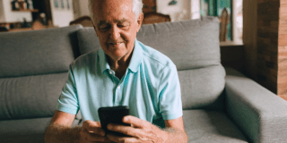 Imagen de un hombre adulto mayor sentado mirando su celular.