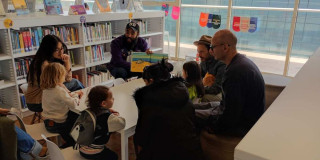 Foto que muestra un grupo de personas y niños sentados en un salón de una biblioteca