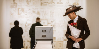 Imagen de uh hombre con sombrero y ramo de rosas mirando uno de artículos de la expo en la FUGA