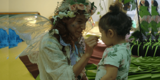 Imagen de una mujer vestida de ada maquillando a una niña de la primera infancia.