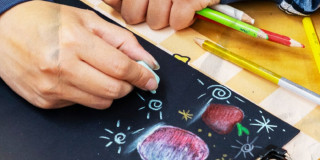 Imagen de una mano con una tiza sobre cartelera negra con dibujos y colores