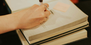Imagen de la mano de una mujer escribiendo en un libro.