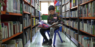 Imagen de un niño leyendo un libro en medio de un stand de libros en las Bibliotecas públicas de Bogotá