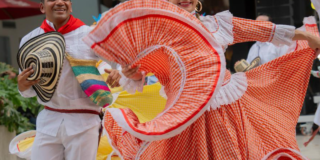 Imagen de un hombre y una mujer que bailan cumbia con sus respectivos trajes típicos.
