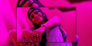 Imagen de " Angelik DK" sentada con gorra y anillos en un fondo rosado