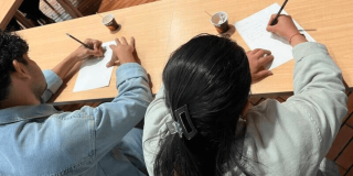 Imagen de dos personas de espaldas escribiendo sobre una hoja