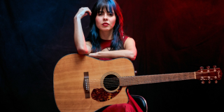 Imagen de la cantante Salie, sentada llevando en sus manos una guitarra.