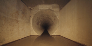 Imagen sobre un espacio de la exposición Katabasis donde se aprecia una pared en concreto beige.
