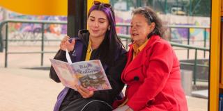 Imagen de una funcionaria de BibloRed leyendo un libro con una usuaria en un Paraderos Paralibros Paraparques de BibloRed