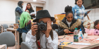 Imagen de niño con una cámara fotografica con personas de fondo en tallerres de manualidades de BibloRed