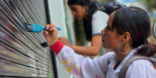 Imagen de dos mujeres jóvenes que pintan la fachada de una casa