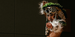 Imagen de un hombre indigena que lleva gorro de plumas en su cabeza.