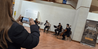 Imagen de una mujer tomando una fotografía con el celular a grupo tocando violines 