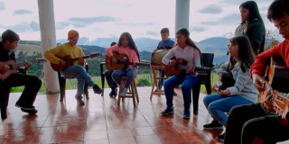 Imagen de varios jóvenes sentados tocando guitarra, de fondo se ve la naturaleza.