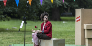 Imagen de una payasa sentanda en un parque que mira tristemente. 