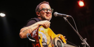 Imagen del cantante César López en un escenario donde lleva una guitarra en sus manos.