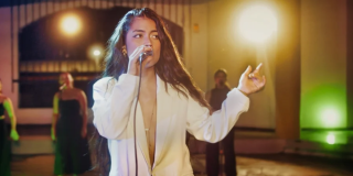 Imagen de una mujer joven de cabello rubio largo cantando con un micrófono.