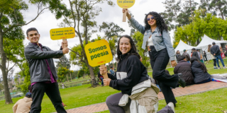 Imagen de dos mujeres jóvenes y un hombre que se encuentran en un parque, en sus manos llevan carteles con info del Festival Reverso.