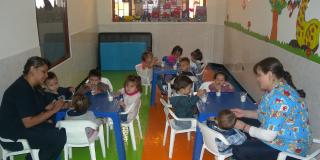 Plano general de un jardín infantil donde dos profesoras atienden a un grupo de niños pequeños.