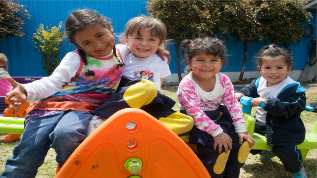 Cuatro niños sonriendo y posando para la cámara, en un parque al aire libre rodeados de juguetes