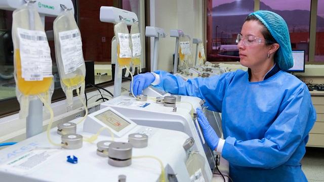 Una mujer con bata, tapabocas y gorro, revisando muestras en un laboratorio 