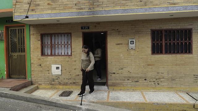 Una mujer saliendo con bastón de su casa que fue beneficiada con el programa