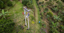 Foto que muestra árboles y dos personas con uniforme de Enel Colombia en un poste de energía 