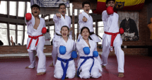 Imagen de dos niñas de rodillas y cuatro jóvenes de pie en posición de karate, todos vestidos con el traje de esta disciplina.