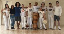 Imagen de varios participantes de una clase de capoeira de los cuales uno de ellos porta un tambor 