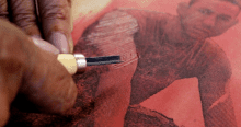Imagen de una mano trabajando el grabado de una imagen de un hombre en una pieza textil 
