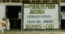 Imagen de fotograma documental 'La Ley del monte' muestra pared pintada con escrito ¨ los pueblos piden justicia¨ y personas de pie de en la puerta