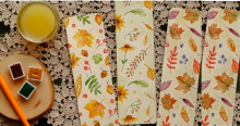 Imagen de una mesa en la que hay unas pinturas, un picnel y tres servilletas con dibujos de flores.
