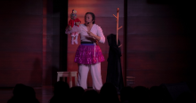 Imagen de los protagonistas de la obra: una mujer joven vestida de balnco con un delantal y un títere femenino con vestido rojo.