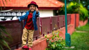 Un niño juega en una baranda, mira a la cámara y extiende su dedo pulgar en señal de aprobación.