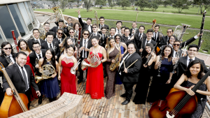 Jóvenes de la Orquesta Filarmónica Juvenil visten trajes formales y sostienen instrumentos musicales.