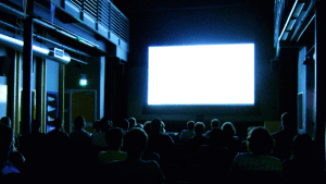 Audiencia en una sala de cine mira una pantalla en blanco.