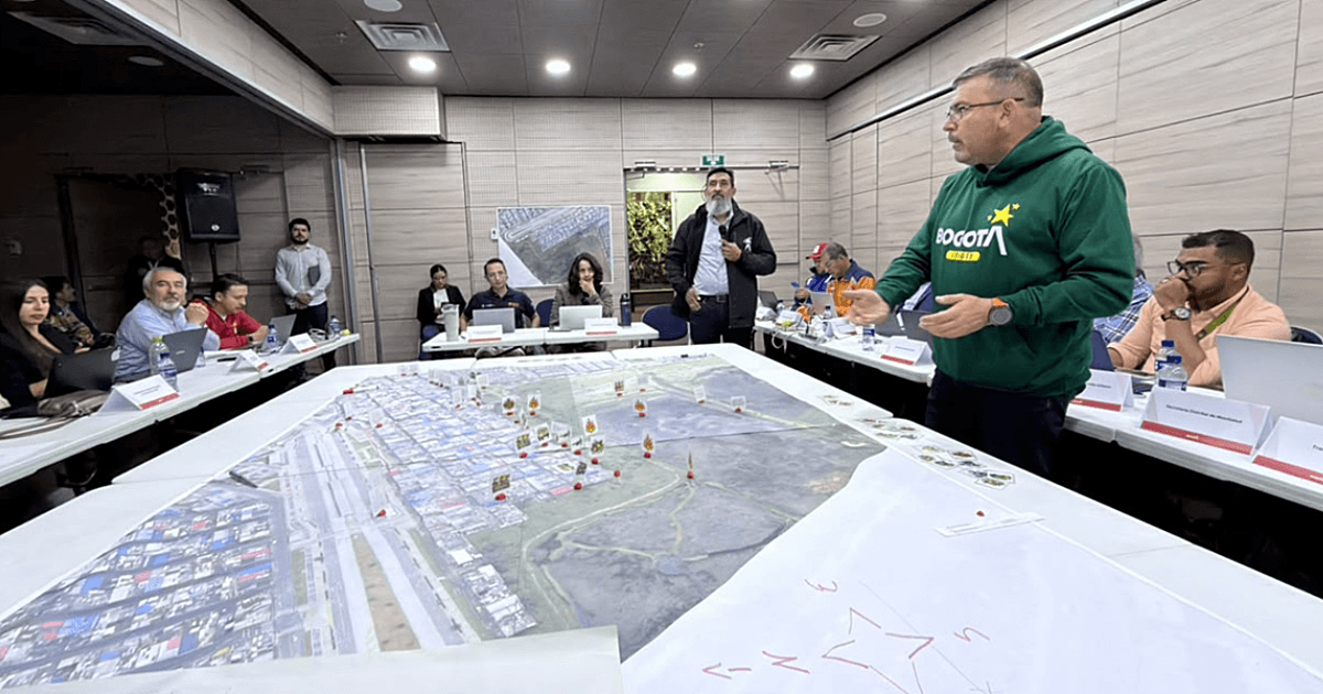 Autoridades distritales participan en simulación de manejo de emergencias alrededor de una mesa con mapas a gran escala, fichas de ubicación y material de planificación.