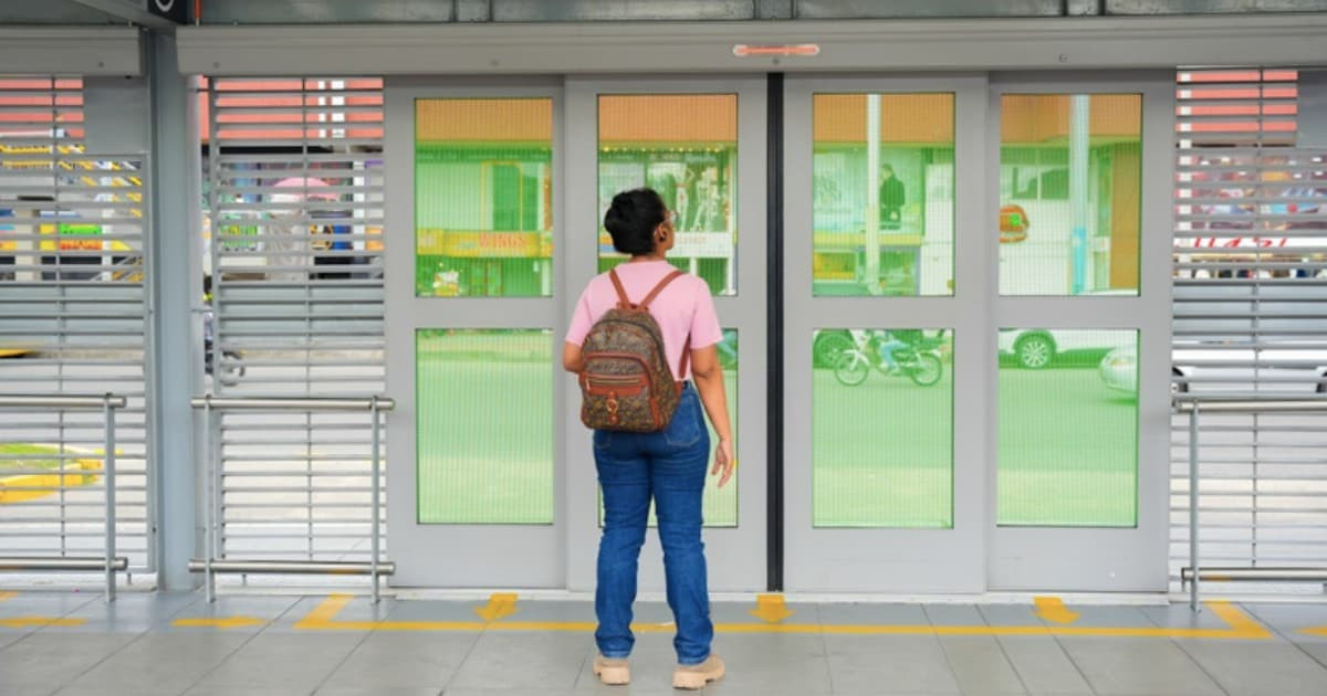 Foto de una mujer en una estación de TransMilenio frente a una de las puertas automáticas.
