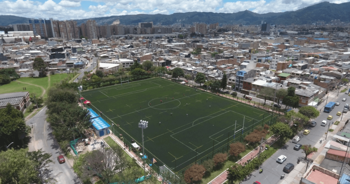 Vista aérea de una cancha sintética de fútbol rodeada por viviendas y edificaciones urbanas en Bogotá.
