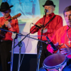 Imagean de unos músicos de orquesta vestidos con camisa roja y sombrero negro, que tocan sus instrumentos