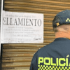 Imagen de un aviso de sellamiento y en primer plano la espalda de un policía