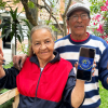 Imagen de dos personas mayores sonriendo y mostrando un celular con la imagen de Ingreso Mínimo Garantizado