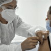 Imagen de una enfermera aplicando una vacuna a una mujer de mediana edad que usa tapabocas