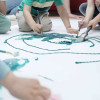 Foto que muestra niños y niñas con pintando en una cartulina con pinceles y pinturas 