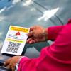 Persona poniendo un volante en el parabrisas de un carro. En el volante se lee: "Notificación de comparendo", con un código QR que invita a escanearse.
