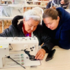 Imagen de una adulta mayor acompañada de una señora cosiendo